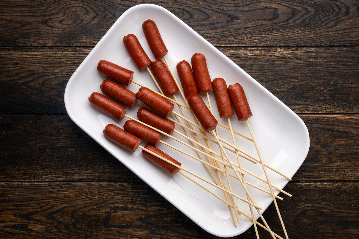 Hot dogs in wooden skewers on a white plate.