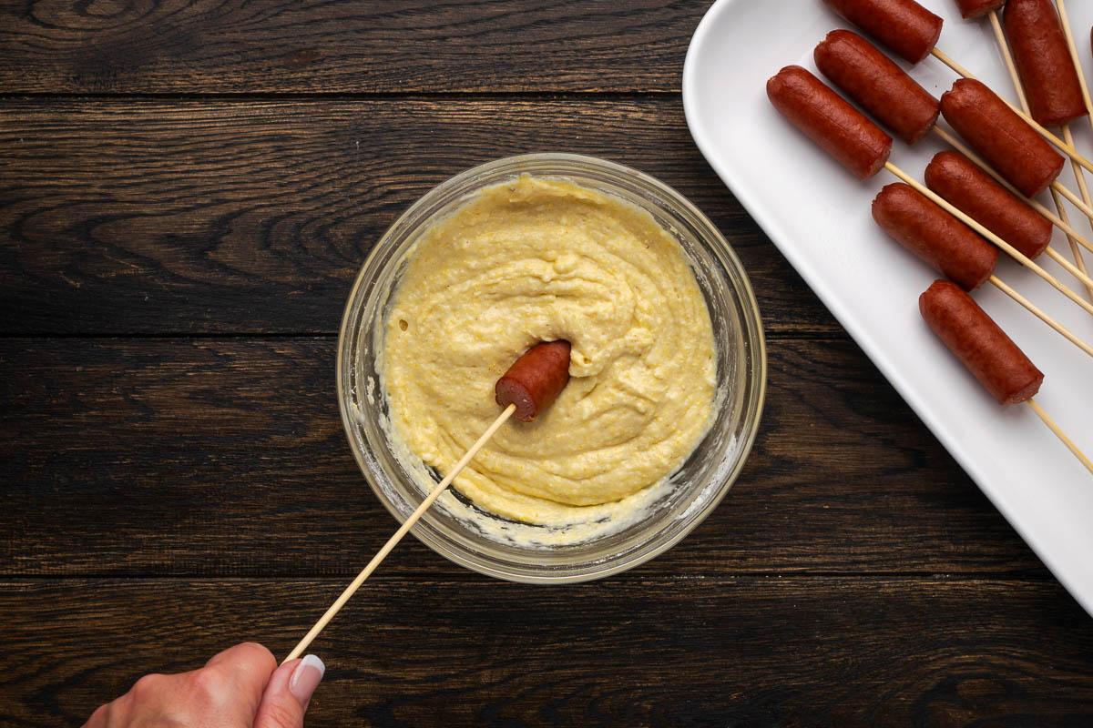 Dipping the corn dogs in a bowl of cornmeal batter.