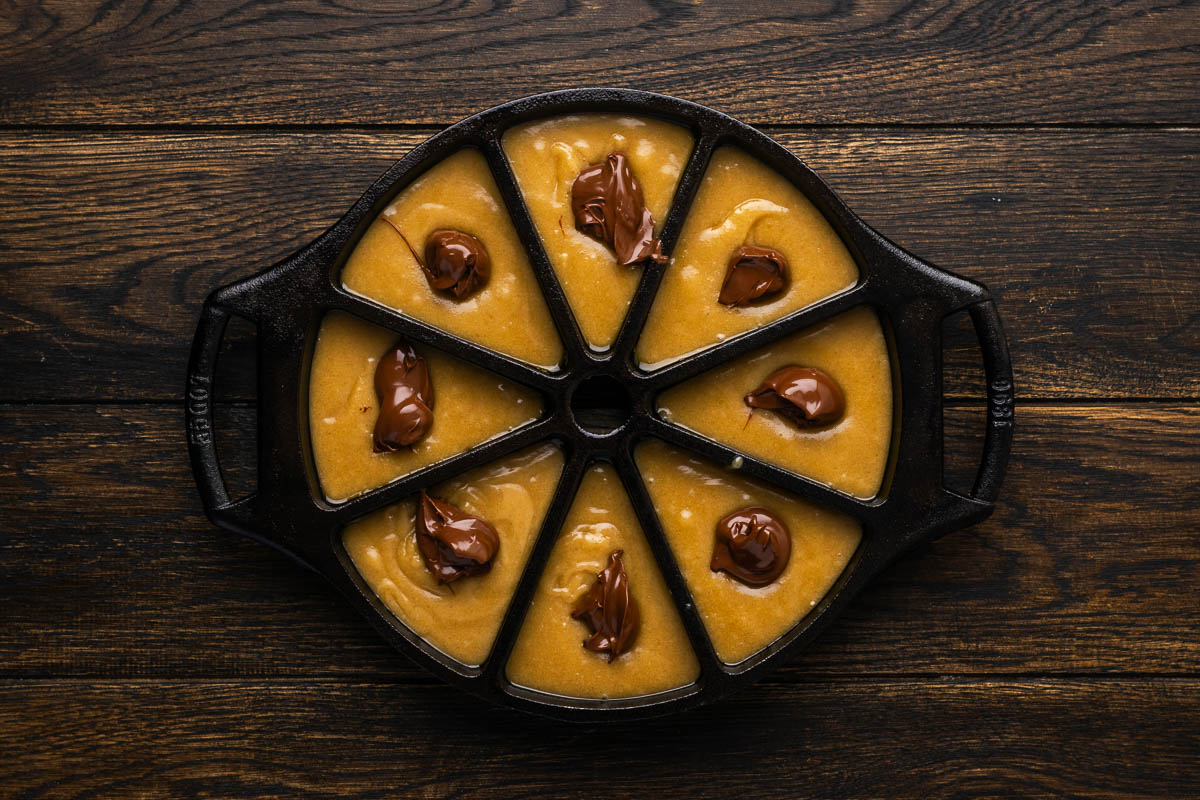 Batter spooned into a cast iron cake mold with nutella added to each. 