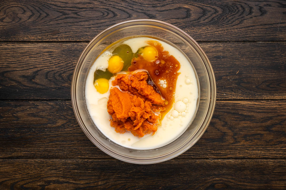 Milk, eggs, pumpkin, and other wet ingredients added to a mixing bowl.