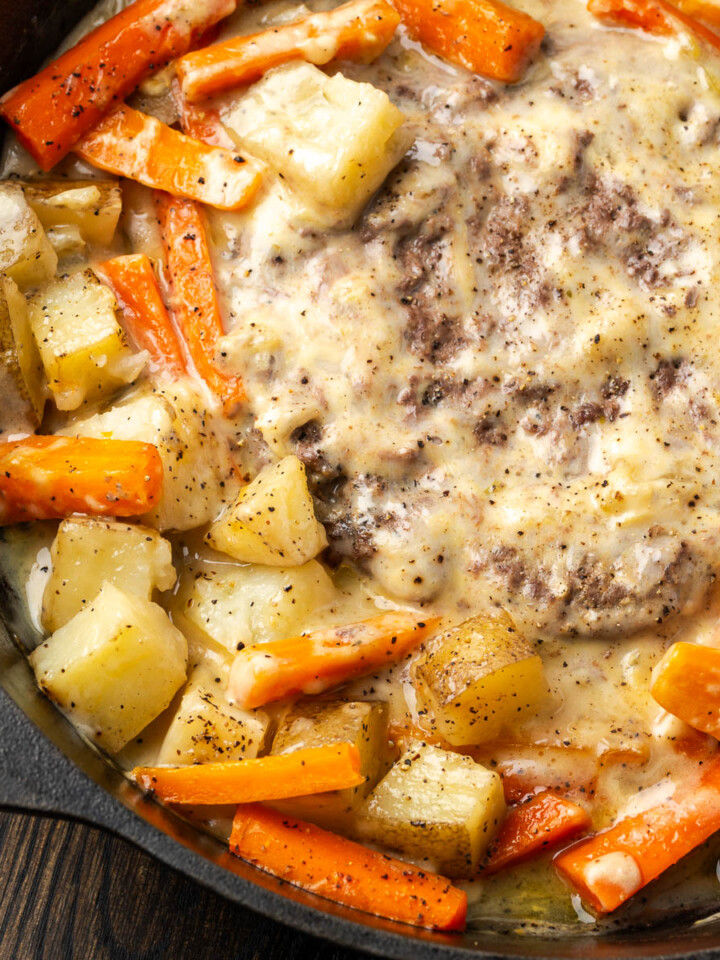 Foil dinner in a skillet with meat in the center and veggies cooked around it.