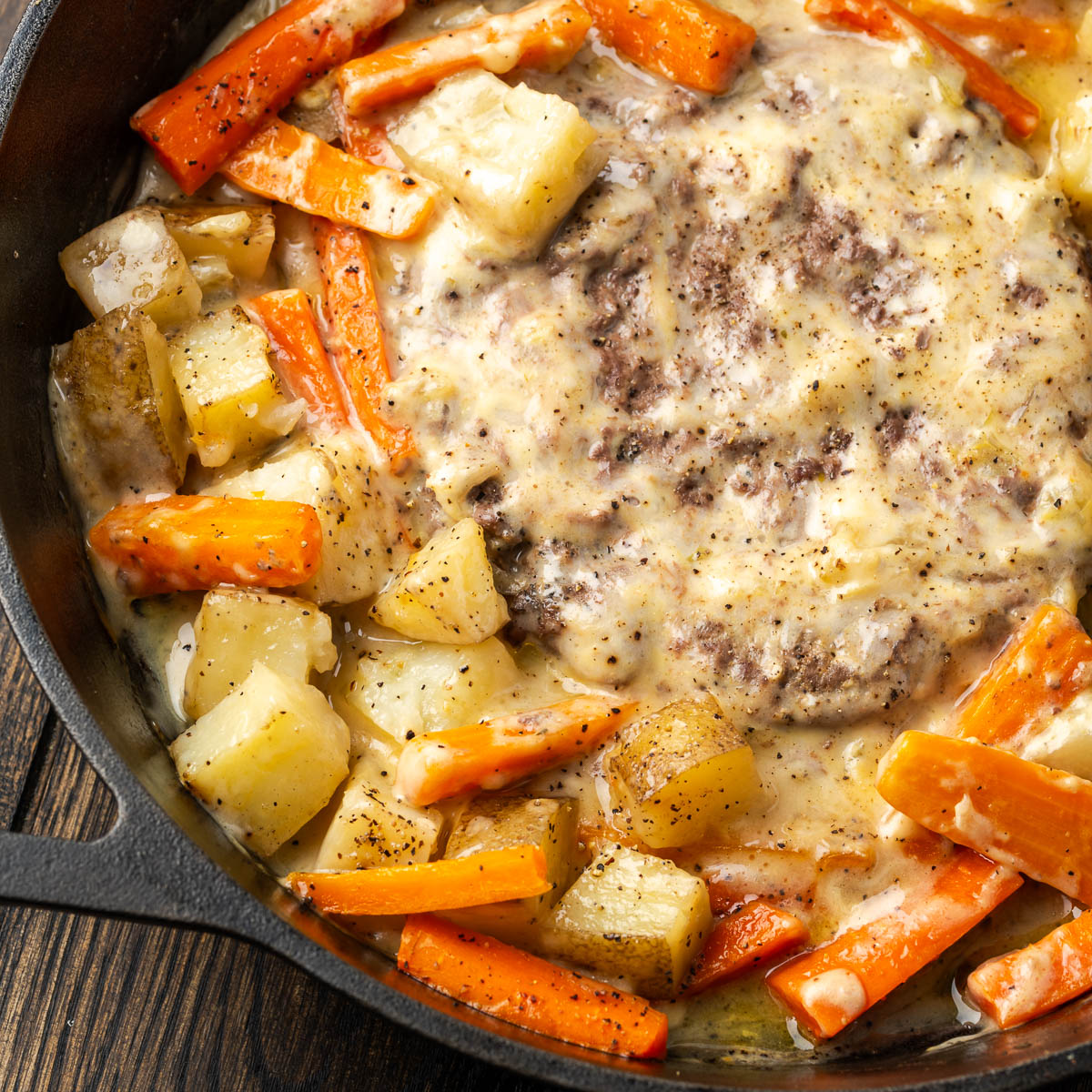 Foil dinner in a skillet with meat in the center and veggies cooked around it.