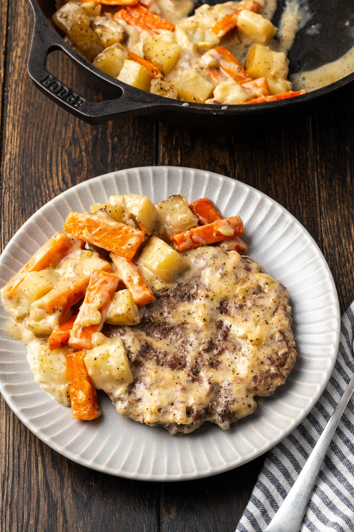 Ground beef and potatoes served on a white plate with more in the skillet in the background.