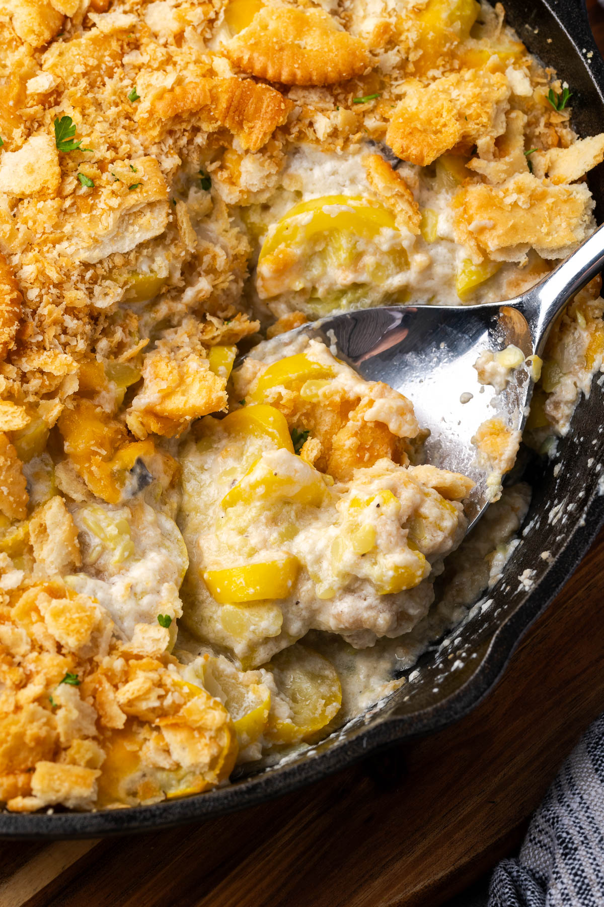 A cast iron skillet of summer squash casserole with a spoon resting in the dish.
