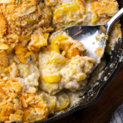 Summer squash casserole in a skillet with a spoon dipping in.