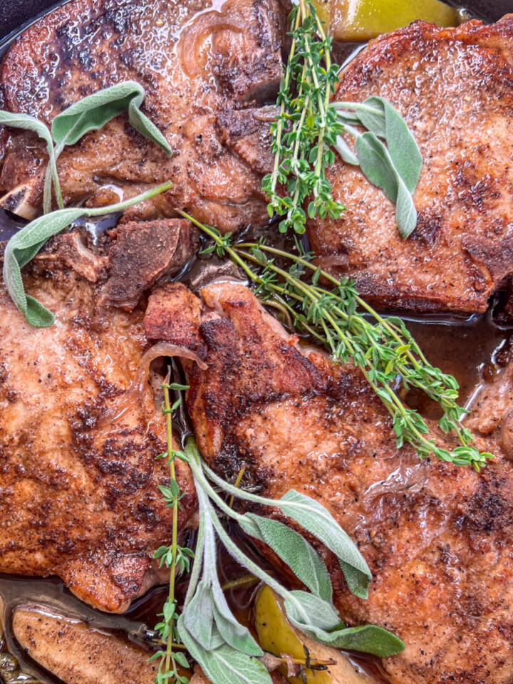 Close up pictures of the cooked pork chops, apples, and onions garnished with fresh herbs.