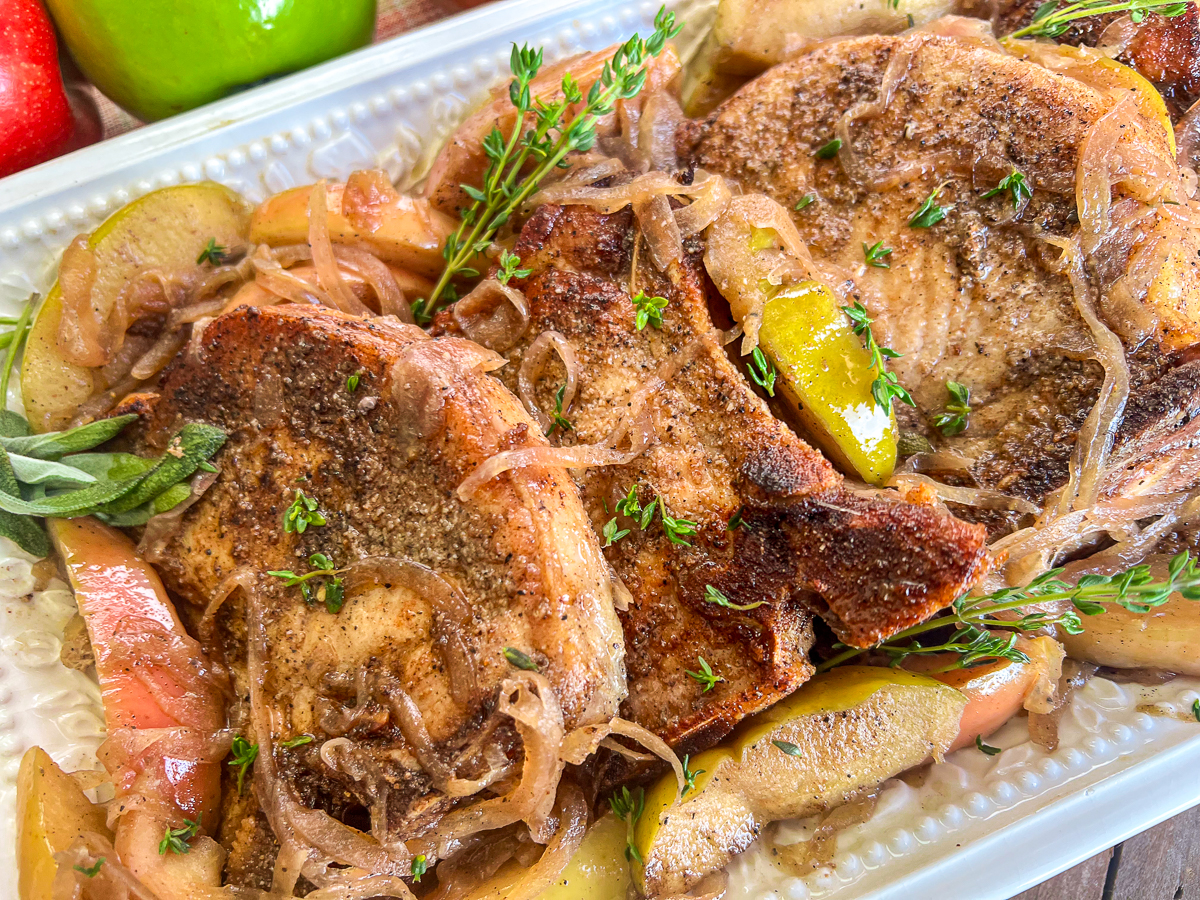 Pork chops, onions, and apples on a white platter.