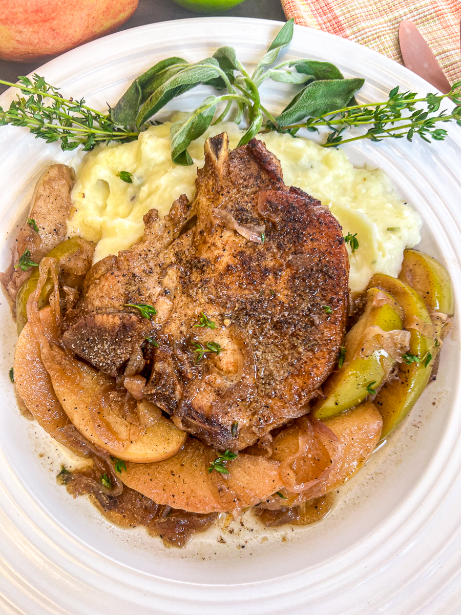 Seared pork chop in a bed of mashed potatoes with apples and onions.