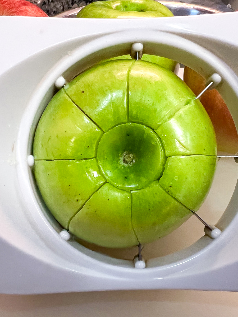 A granny smith apple being sliced with an apple slicer.