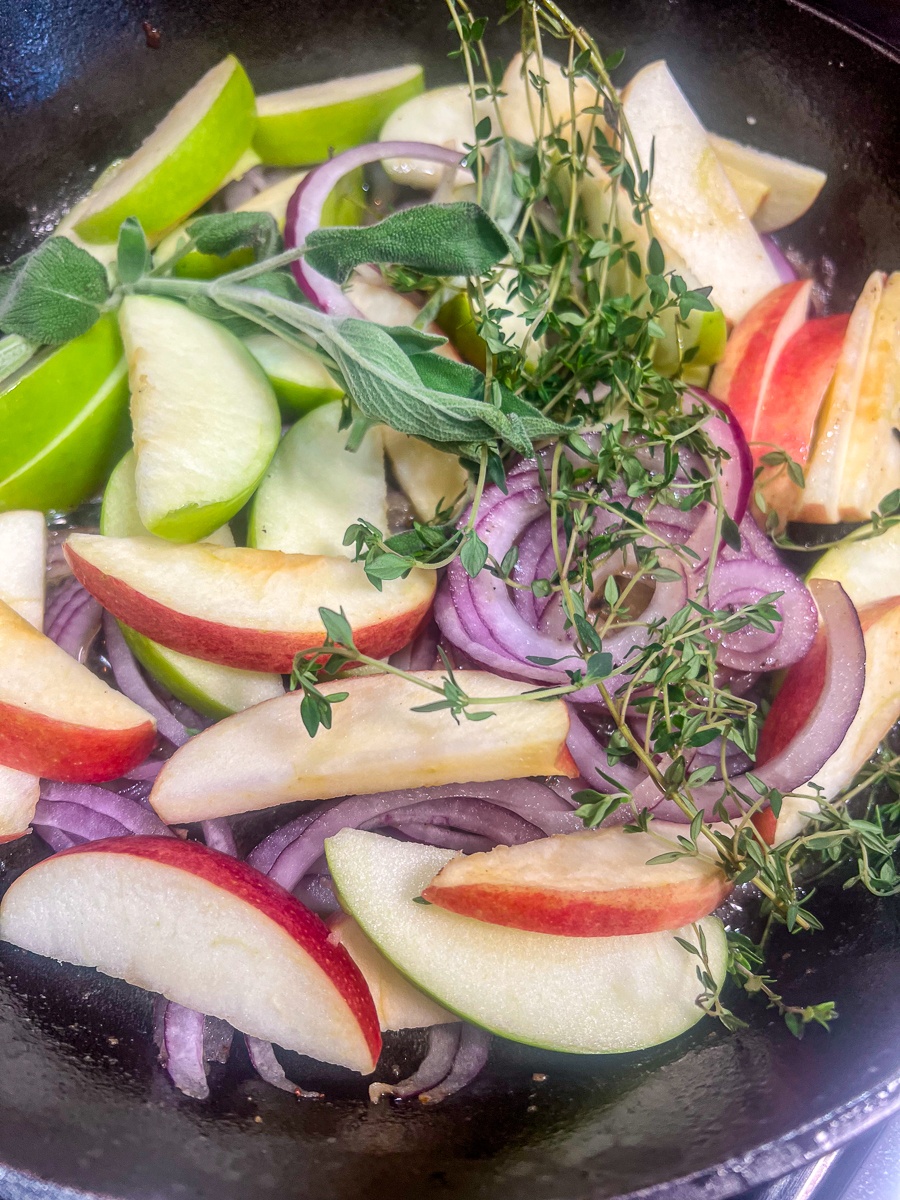 Apples, onions, and herbs in a cast iron skillet.