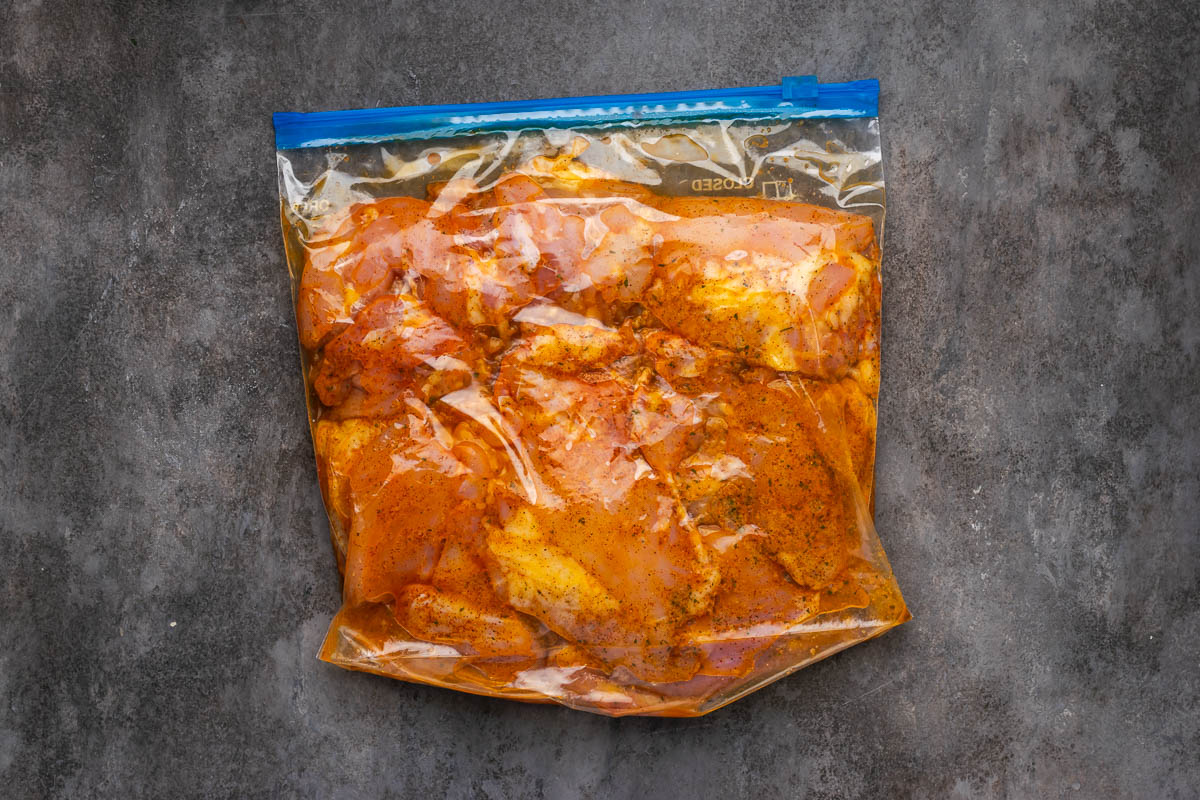 Chicken thighs marinating in a plastic bag with seasonings.