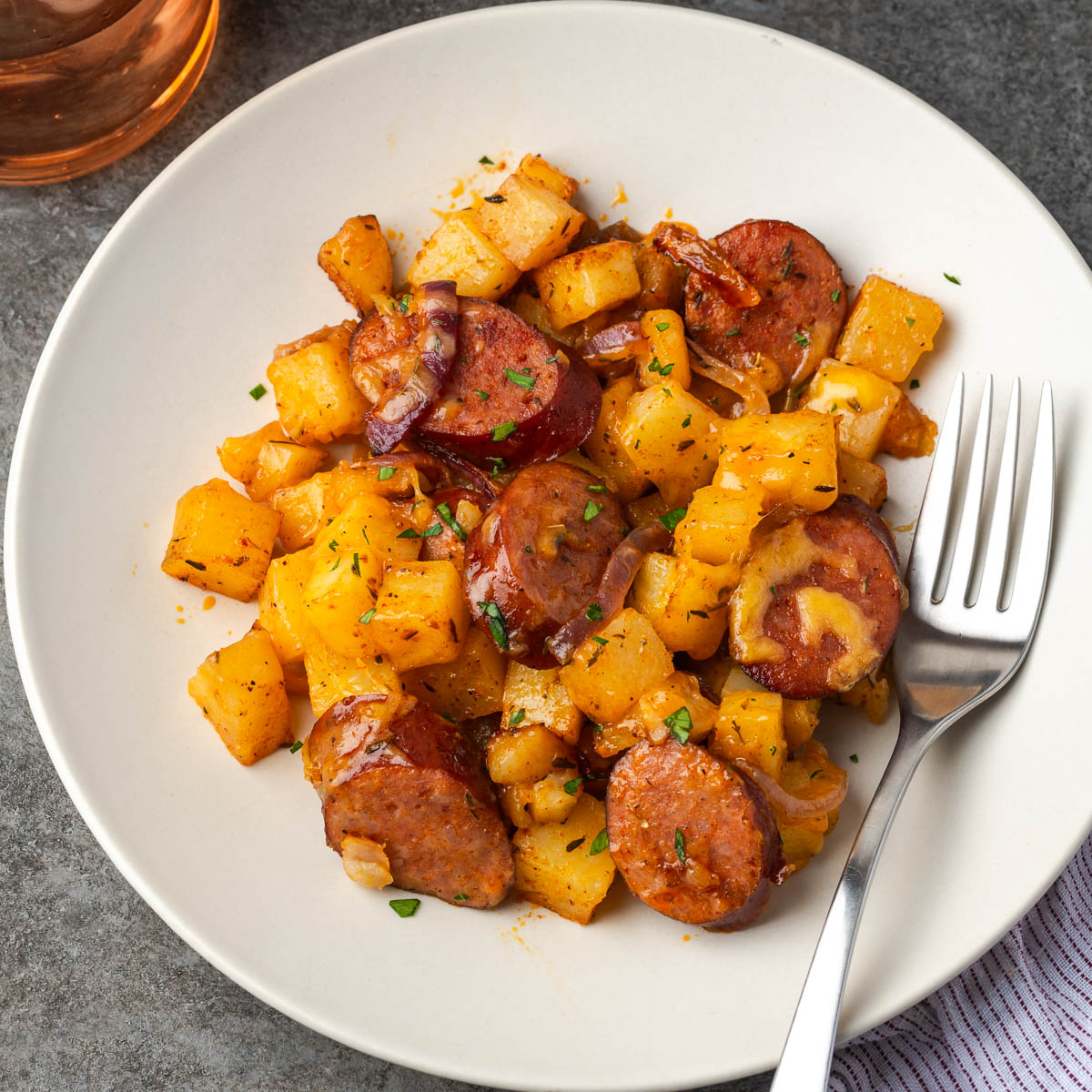 A plate of smoked sausage and potatoes with a fork resting to the side.