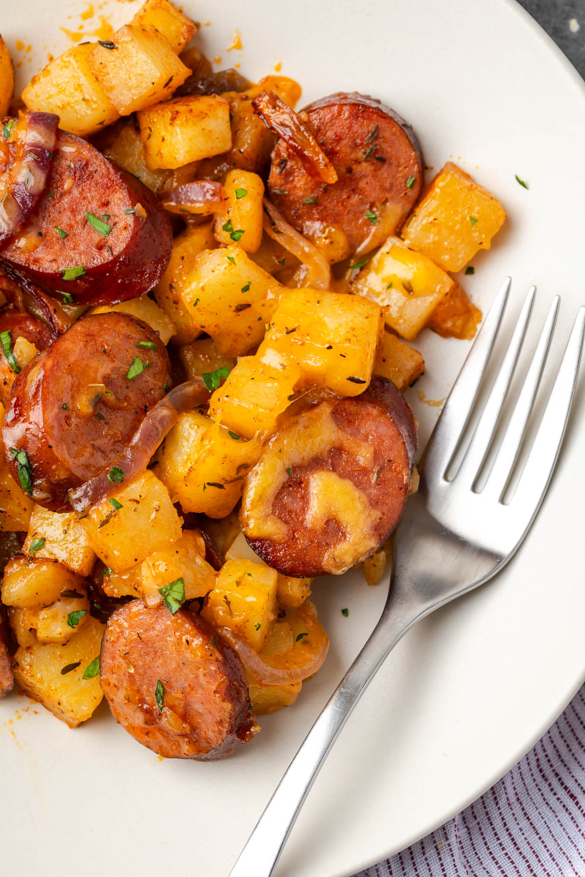 Cheesy sausage and potatoes served up on a plate with a fork resting to the side.