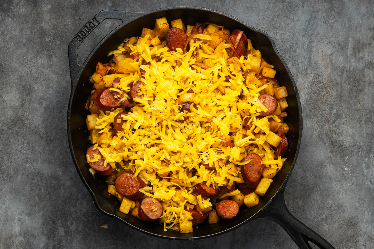 Cheese sprinkled over the top of the potatoes and sausage.