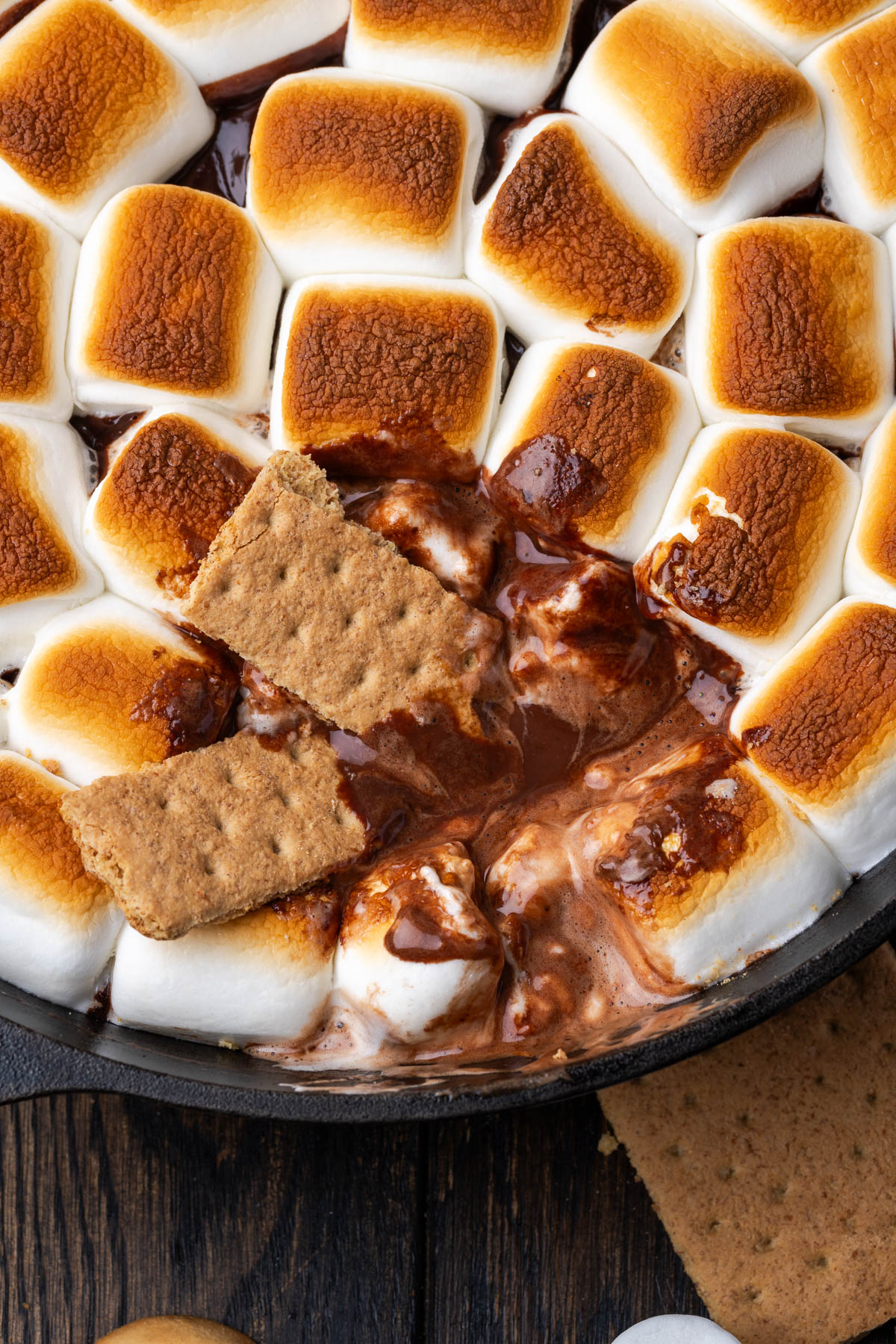 S'mores dip in a cast iron skillet with a graham cracker dipping in.