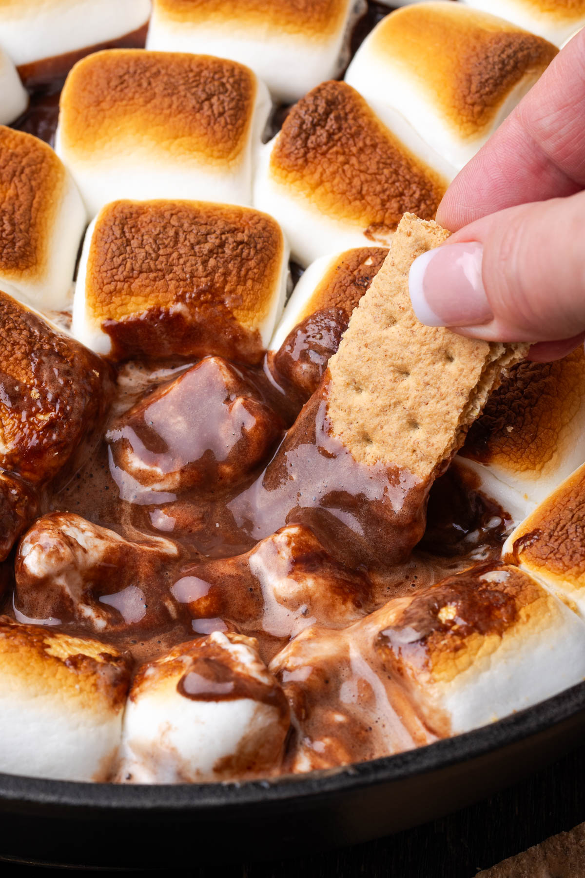 A hand dipping a graham cracker into some s'mores dip.