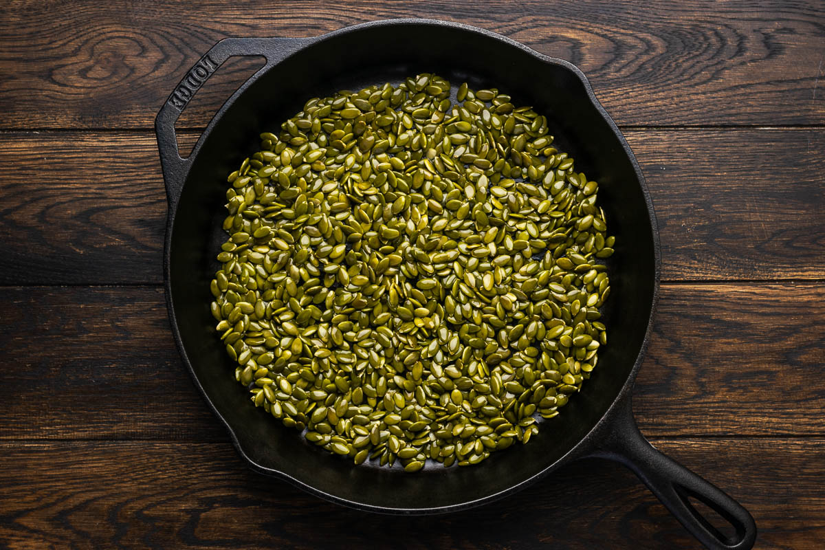 Pumpkin seeds added to a skillet.