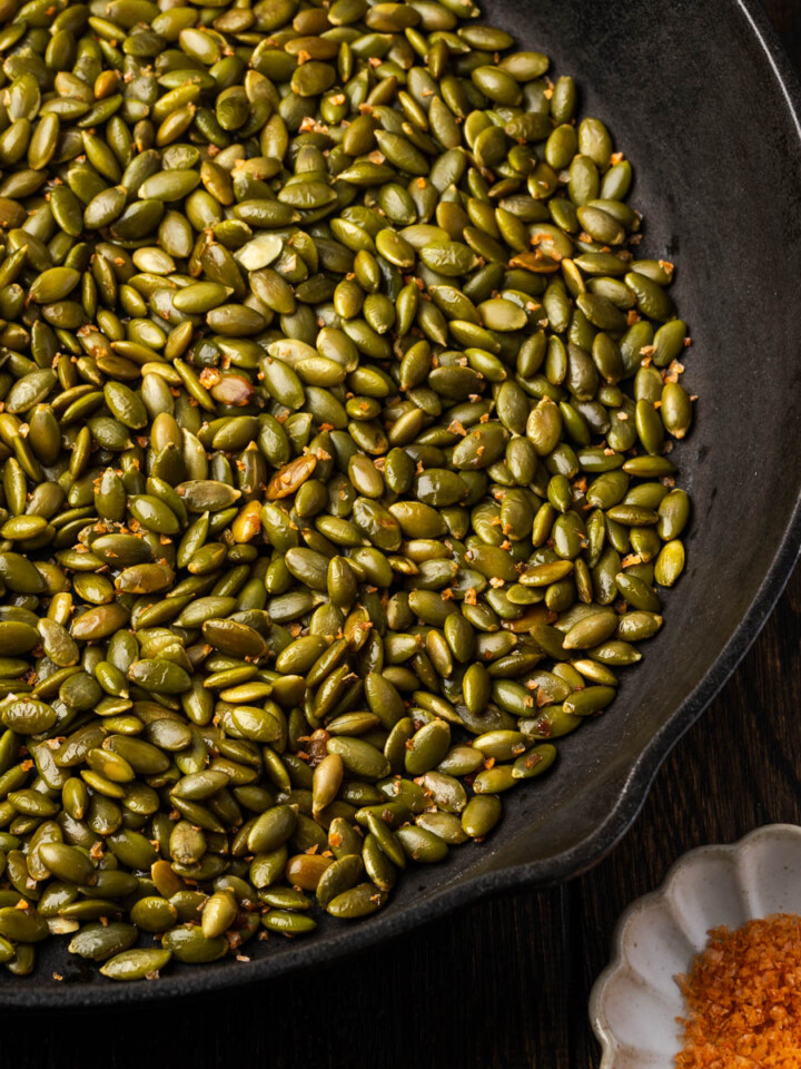 Spiced pepitas in a skillet with a bowl of spicy salt to the side.