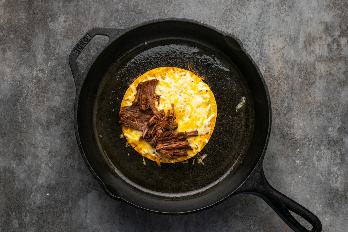 Tortilla cooking in a skillet with beef and cheese on it. 