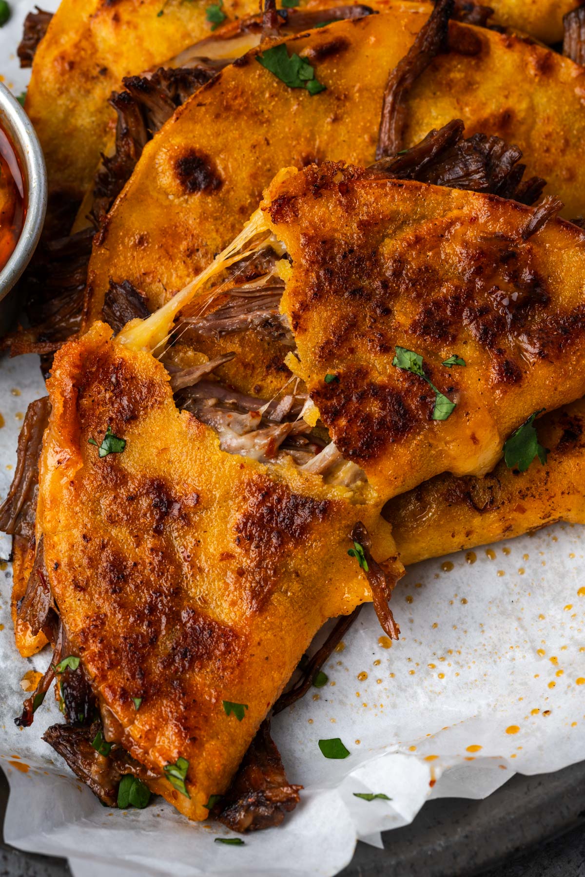 Birria taco broken in half leaning on other tacos.