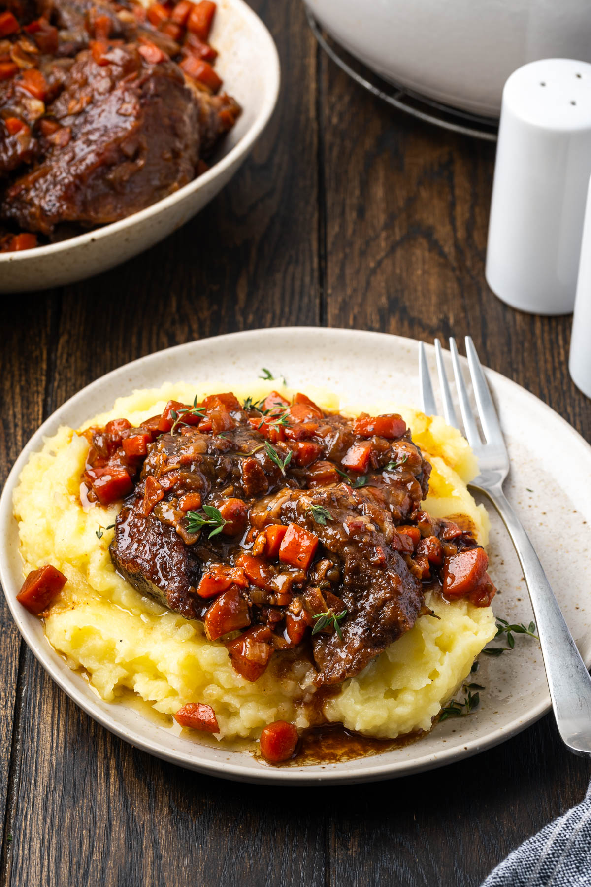 A plate full of mashed potatoes and short ribs with a fork.