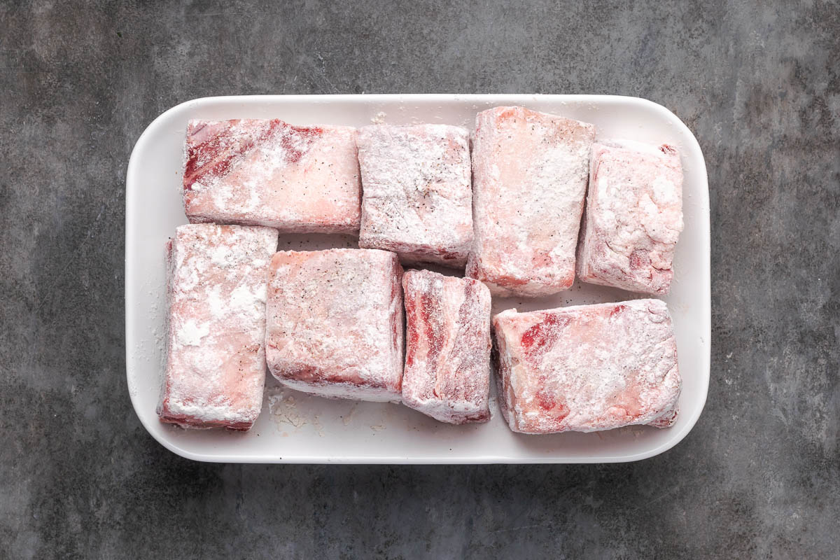 Beef ribs with salt and pepper, and dredge them lightly in flour.