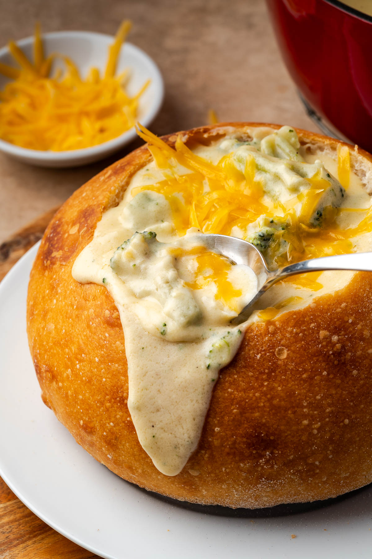 Broccoli cheese soup served in a bread bowl with a spoon scooping some out.