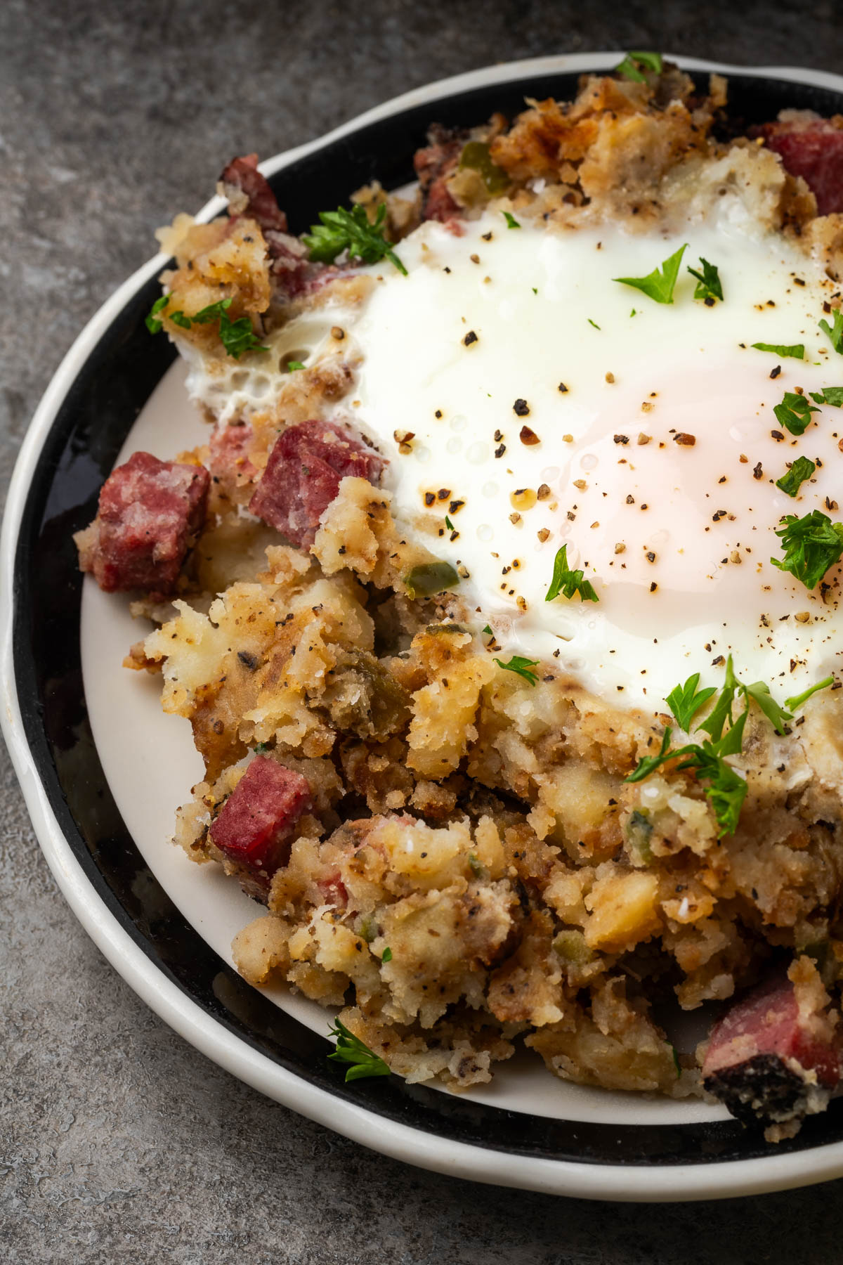 A plate of potato hash with pastrami and egg on top.