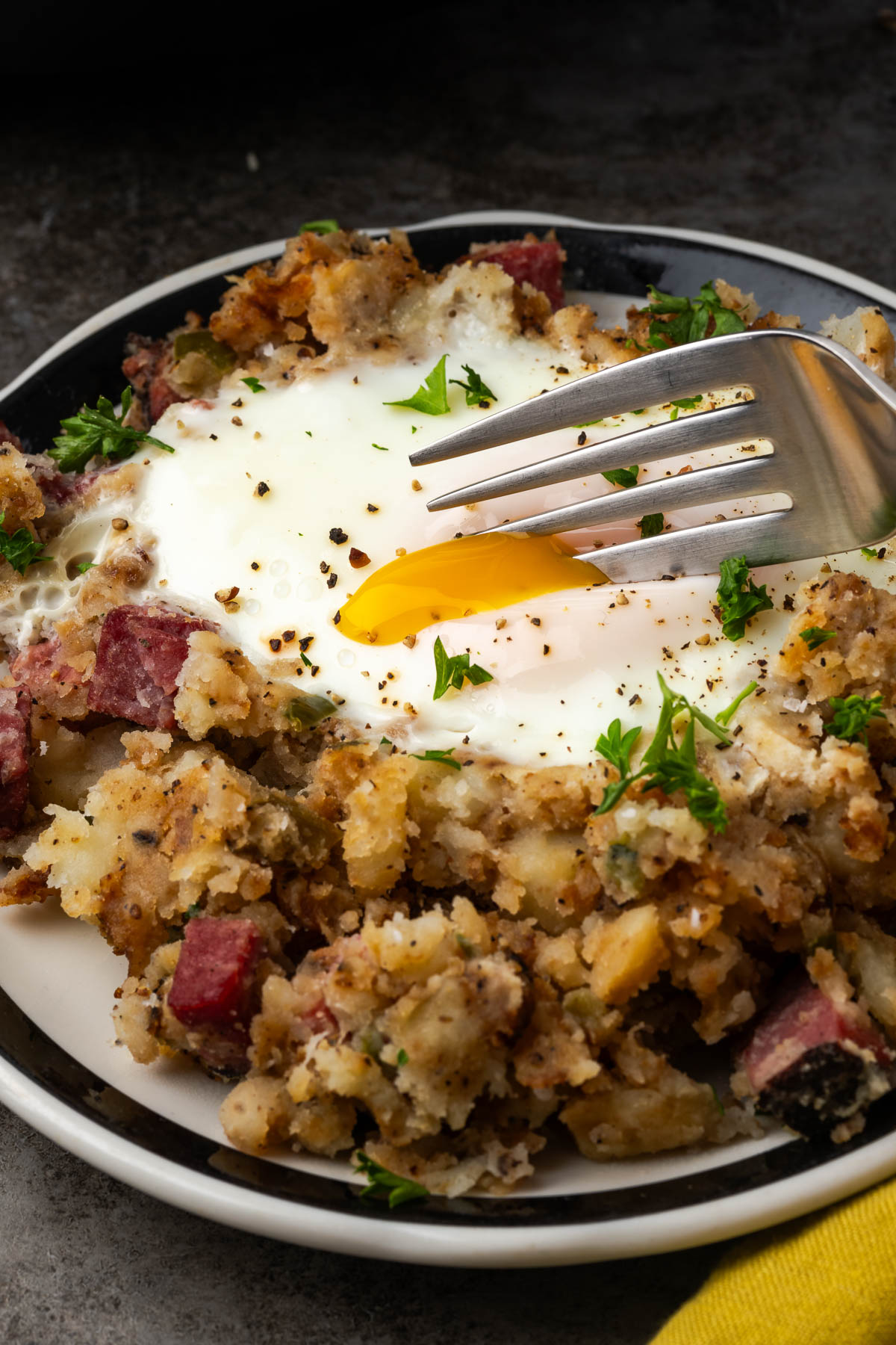 Hash browns with pastrami and a egg yolk cracked with a fork.