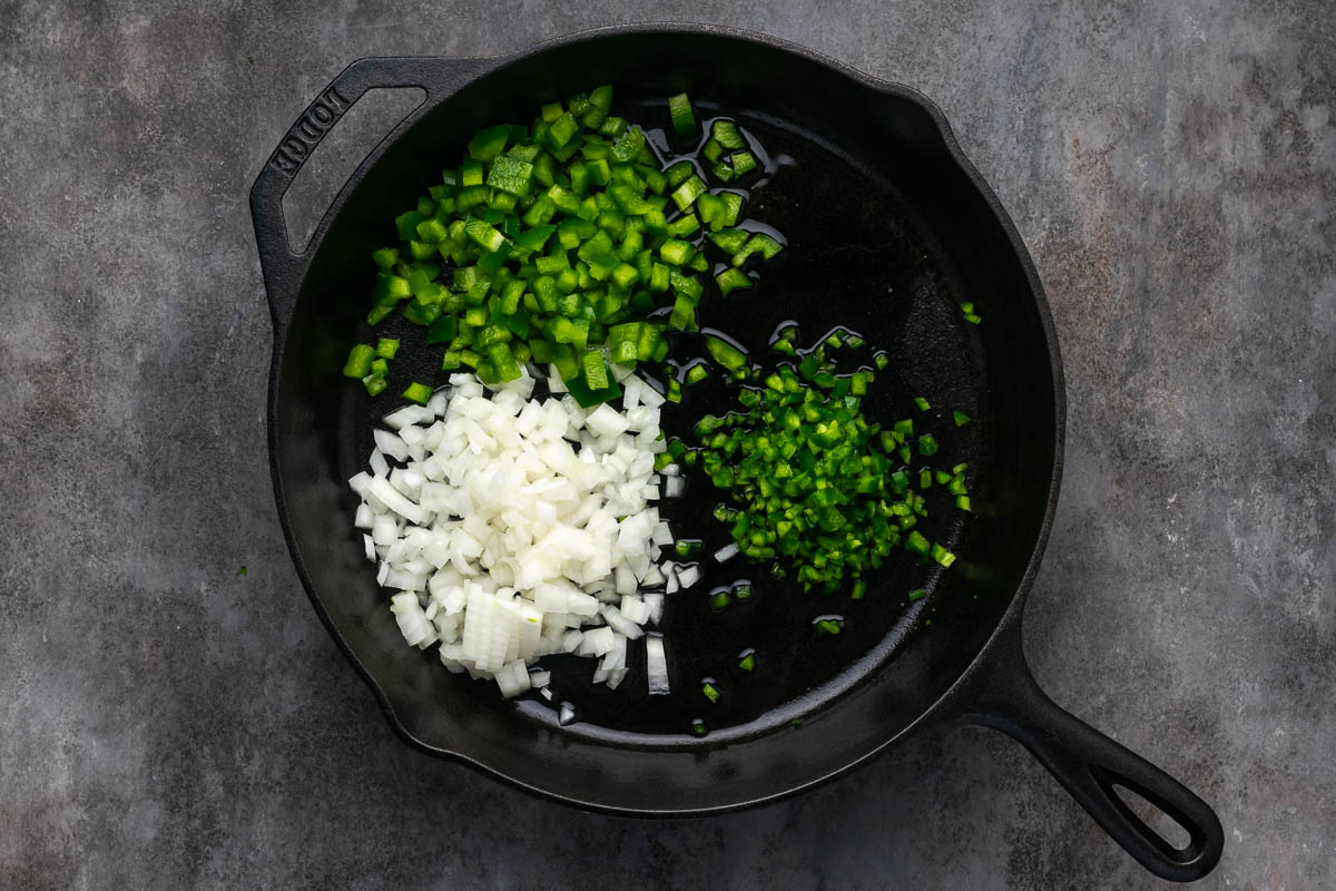 Diced onion, a diced bell pepper, and a minced jalapeño browning on a skillet.