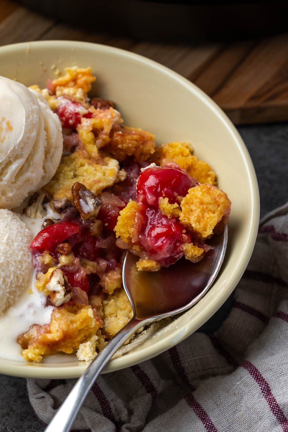 A spoon scooping some pineapple dump cake with cherries out of the bowl.