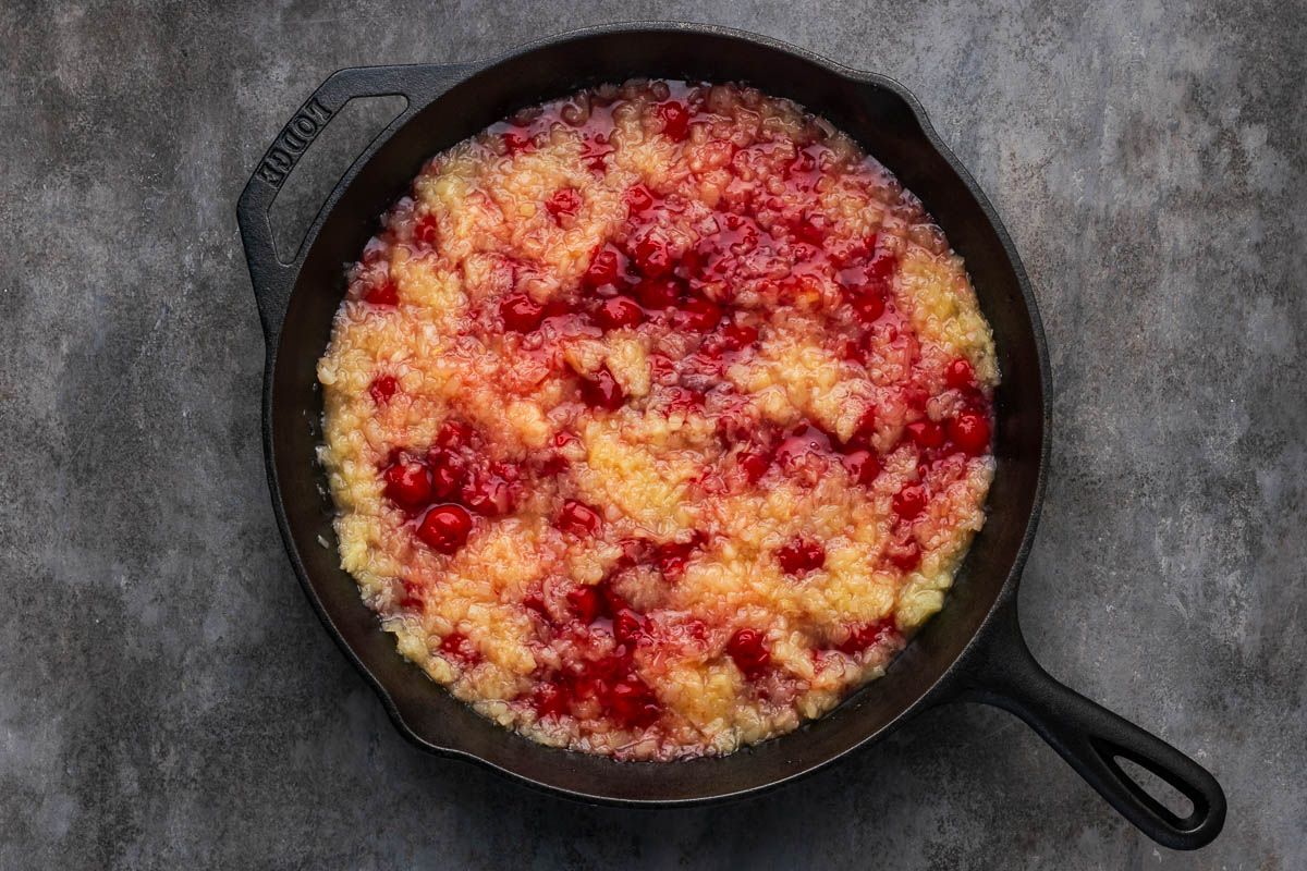 Pineapple chunks and cherry pie filling layered in a dutch oven.