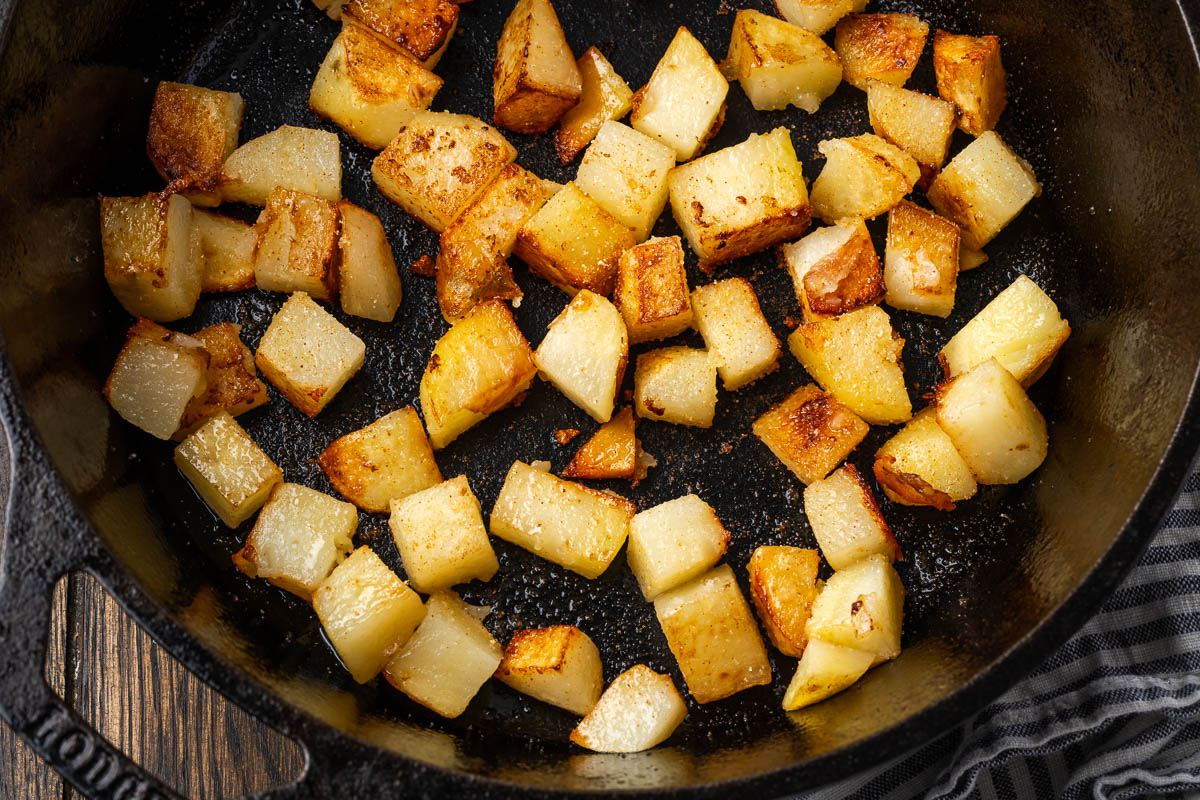 Potatoes flipped and cooking in a skillet.