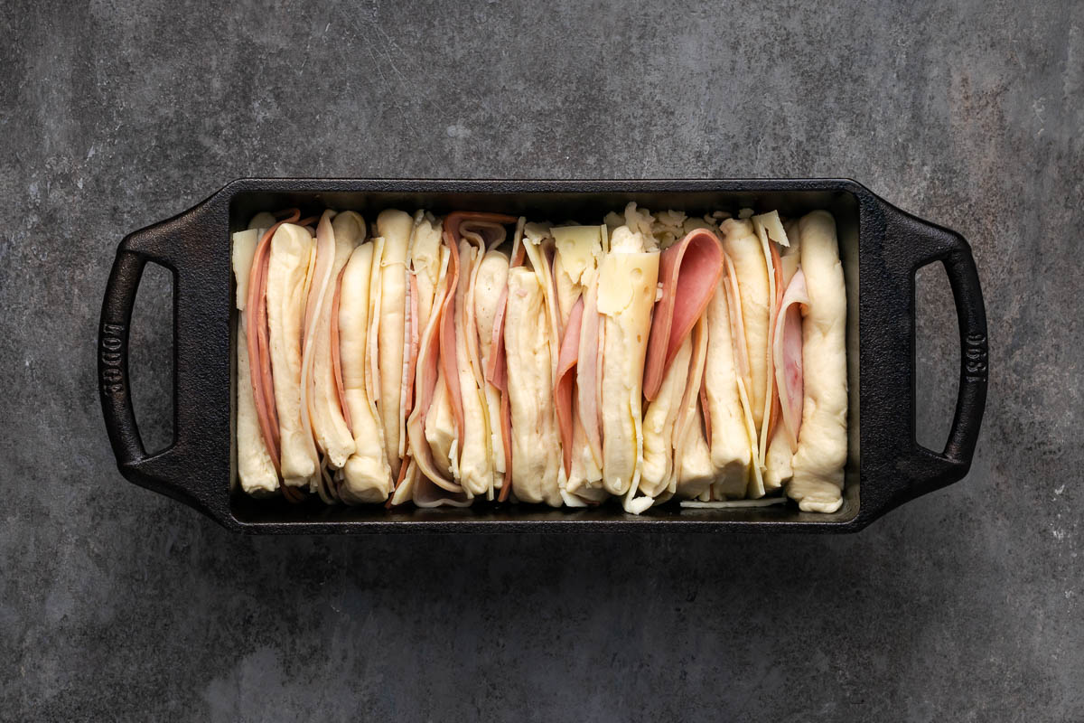 Swiss cheese, ham, turkey and dough layered in the pan.