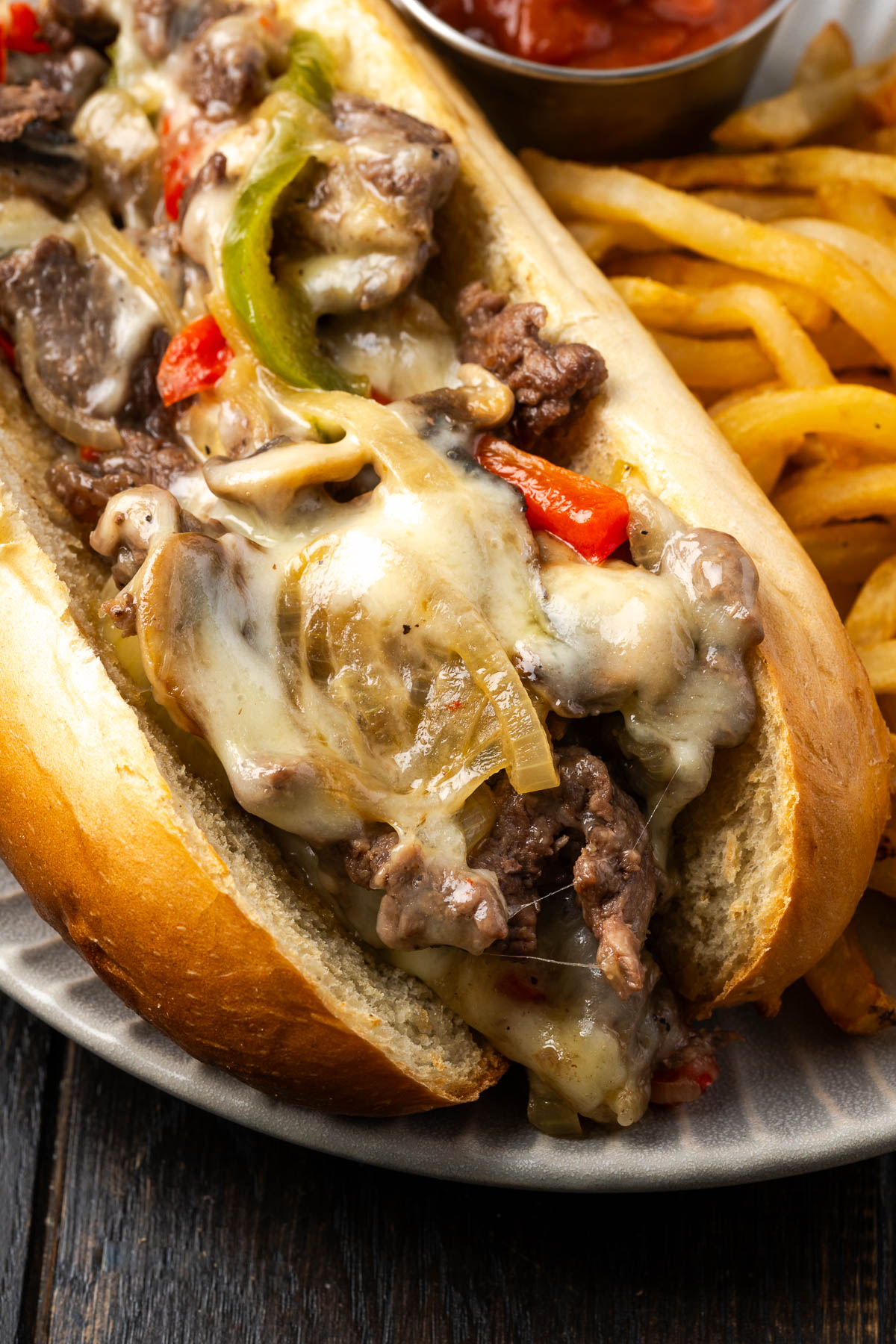 A cheesesteak with peppers, onions and mushrooms on a roll.