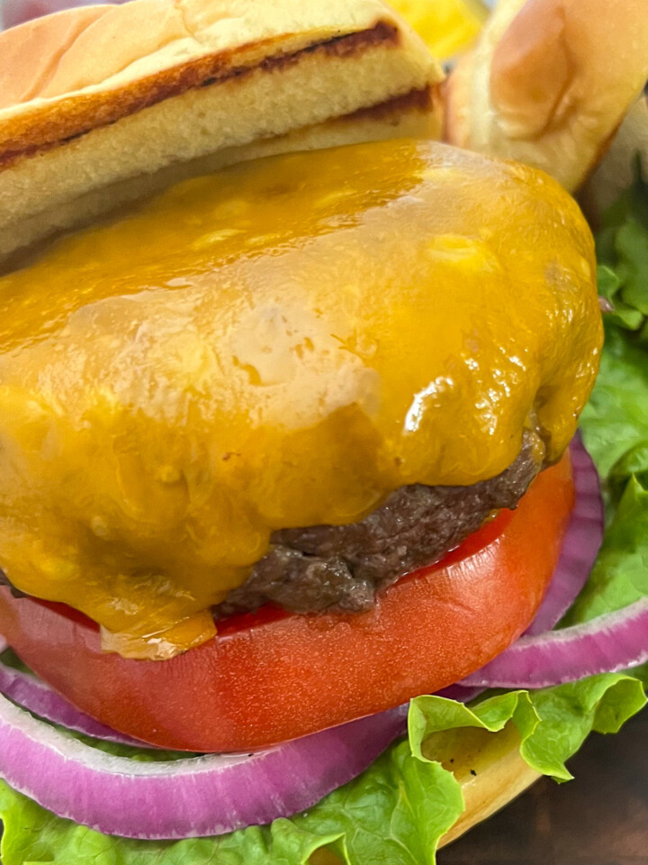 Cast iron burgers on a plate topped with cheese and a bun half off the top.