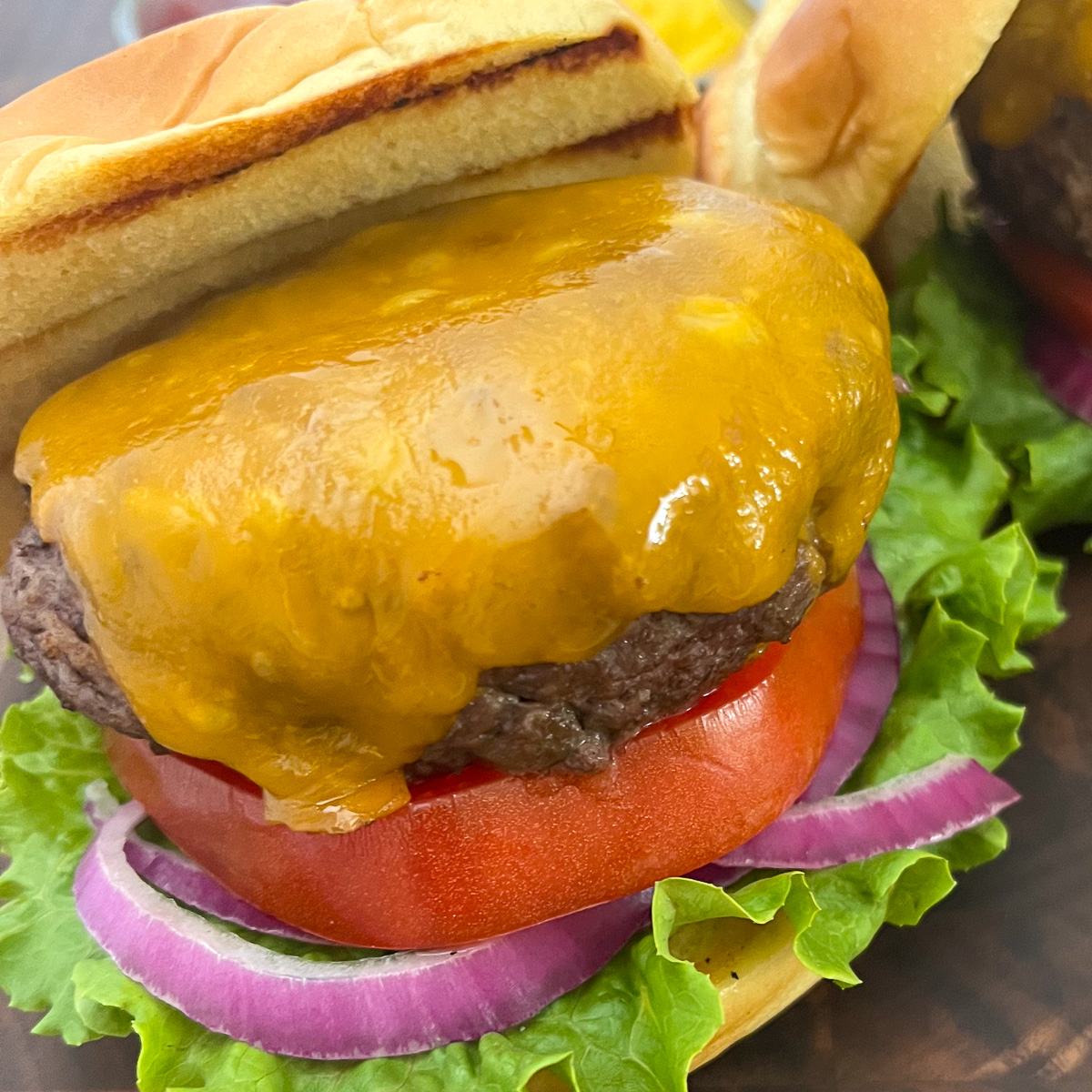 Cast iron burgers on a plate topped with cheese and a bun half off the top.