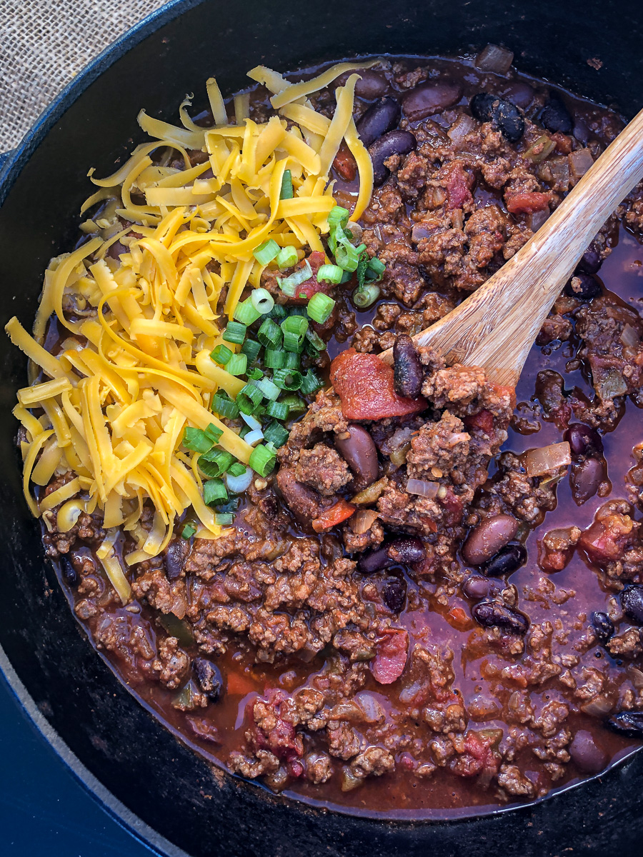 A pot of Dutch oven chili garnished with cheese and chives.