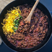 Dutch oven chili in the pot sprinkled with cheese and green onions.
