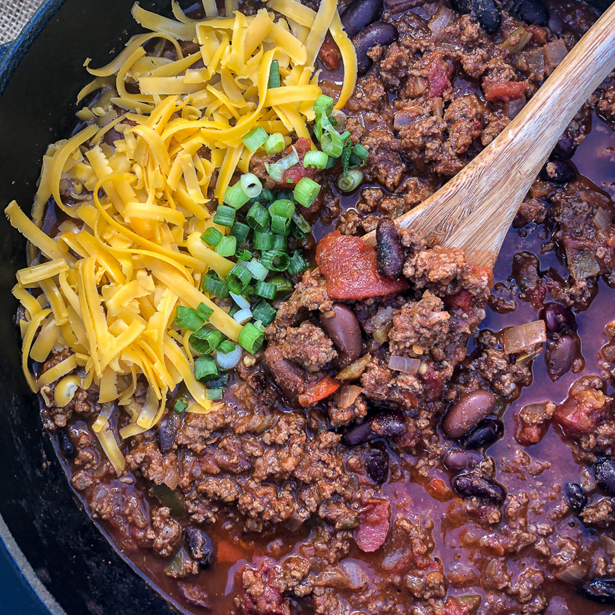A pot of Dutch oven chili with a wooden spoon in the pot.
