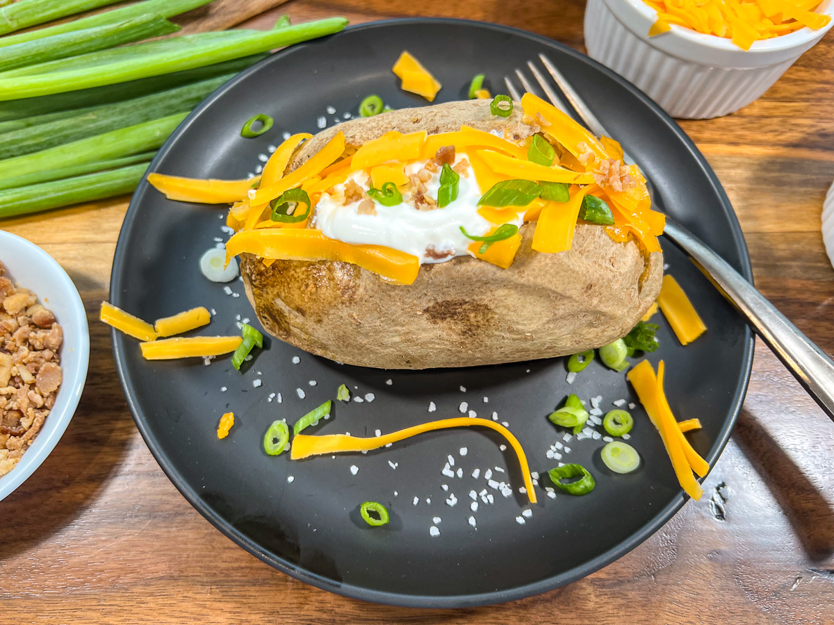 A Dutch oven baked potato cooked over a campfire on a plate.