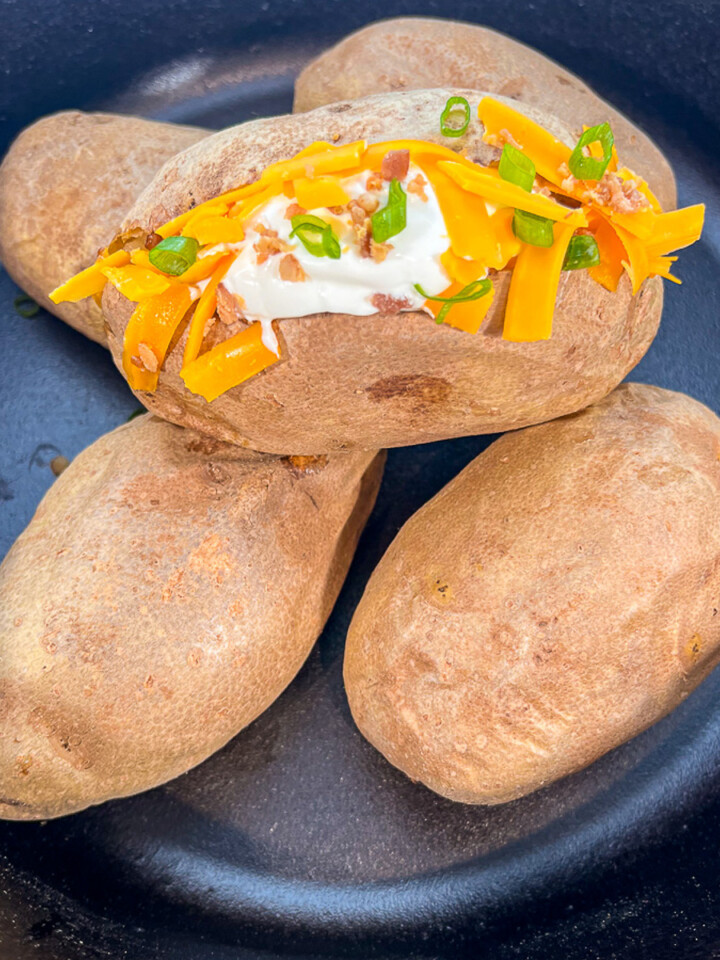Dutch oven baked potatoes with the one on top garnished with sour cream and cheese.