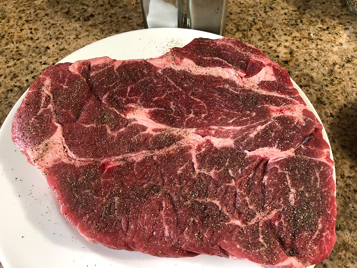 Chuck roast on a plate with seasonings added.