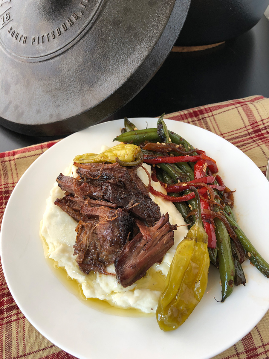 Dutch oven Mississippi pot roast over some mashed potatoes on a plate.