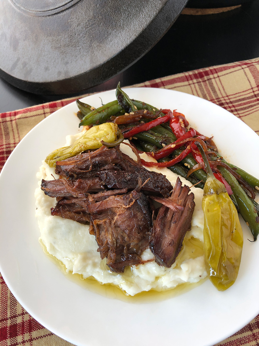 Mississippi pot roast in a Dutch oven served on a plate with mashed potatoes.