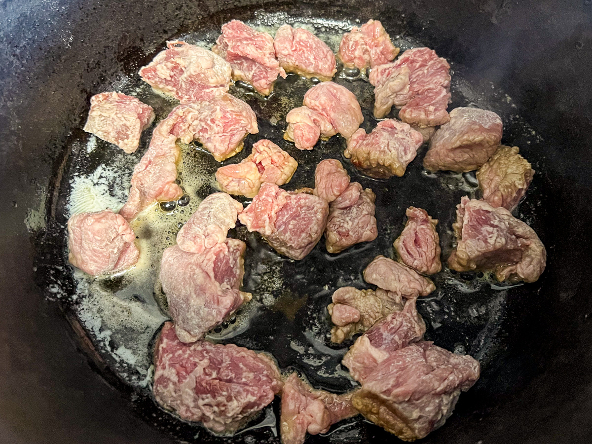 Beef searing in a skillet to make beef stroganoff in a Dutch oven.