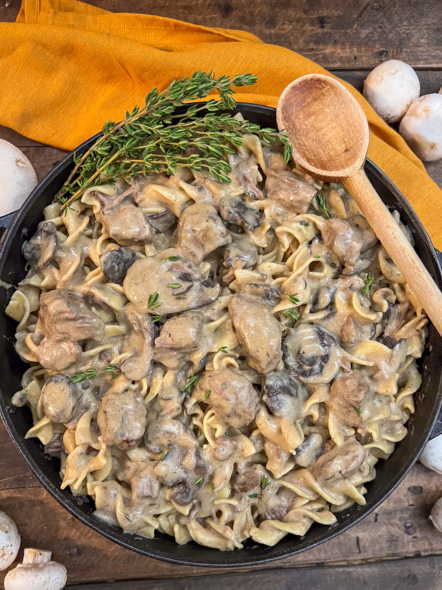 A skillet of Dutch oven beef stroganoff with a wooden spoon resting on the edge. 