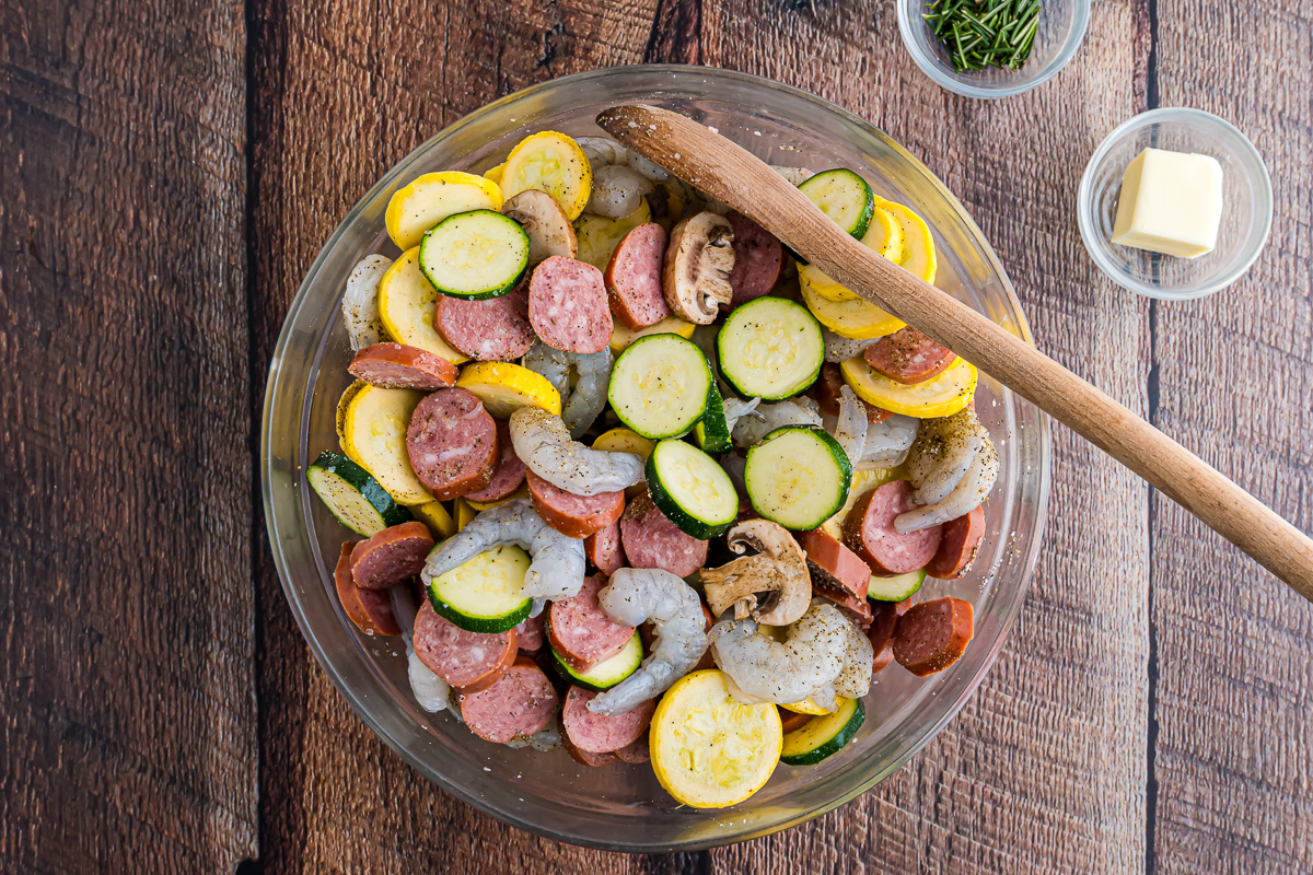 Shrimp, sausage, zucchini, squash, mushrooms, and seasoning salt mixed in a bowl.
