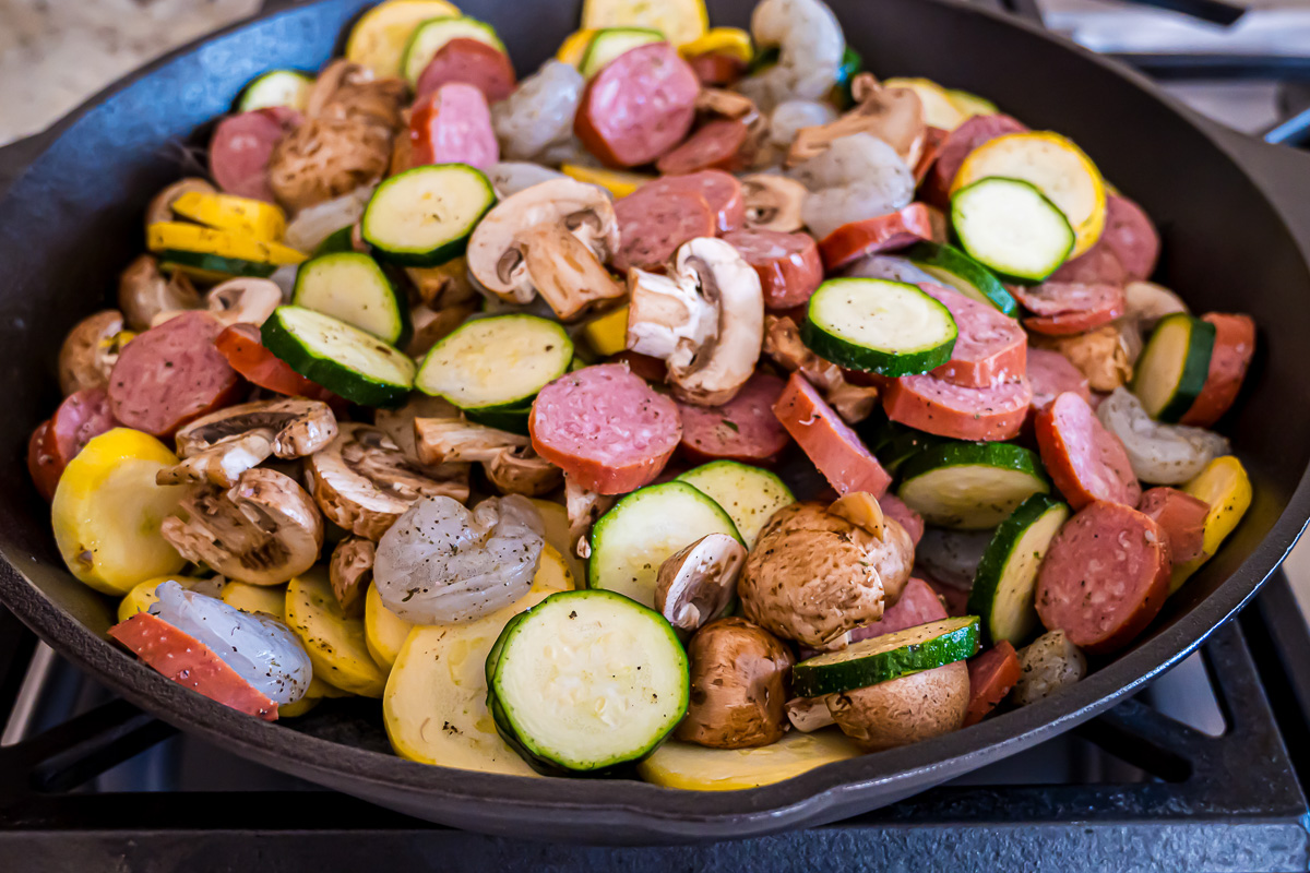 Shrimp, sausage, zucchini, squash, mushrooms, and seasoning salt mixed in a skillet.