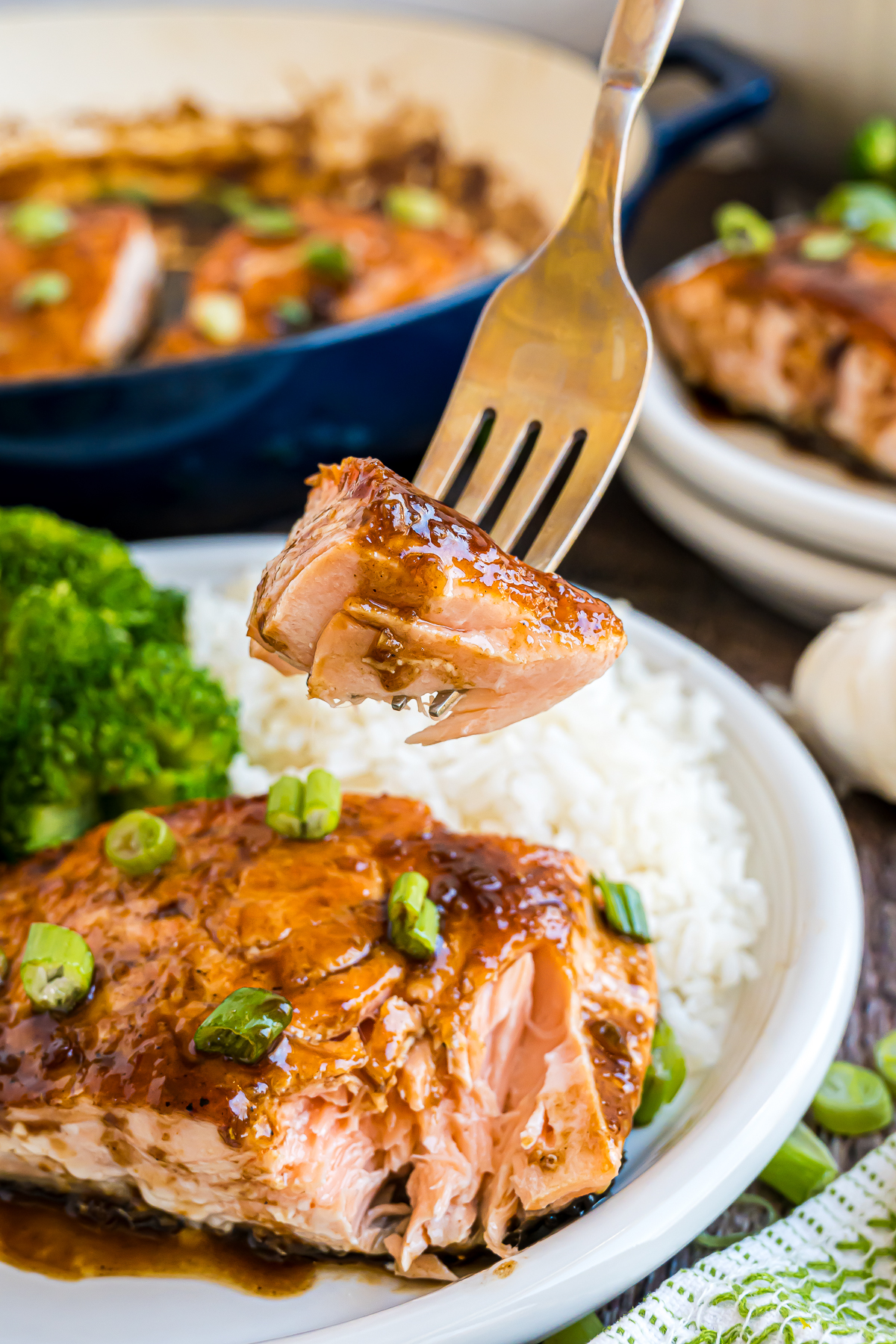A piece of pan seared salmon on a fork held up over a plate of more.